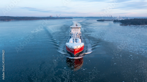 LNG powered oil and chemical tanker making way ahead in Finnish archipelago during winter morning sunrise. Haze in the air and sea surface covered in light ice floes. Aerial front view photo