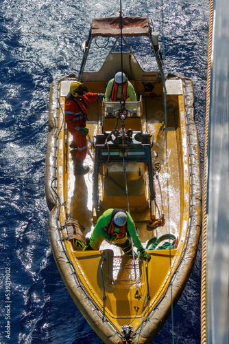 Top down view of launching or recovering orange Fast Rescue Boat (FRC) from ship with three crew members onboard. FRC is used in search and rescue missions and man overboard situations. photo