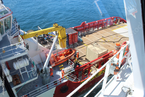 Red hulled standby safety vessel in ship to ship operation. It is used to refuel and resupply seismic survey vessels during oil and gas exploration.