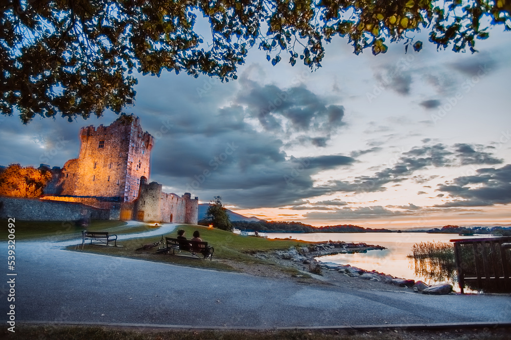 Ancient old Fortress Ross Castle ruin with a lake, green grass and orange clouds. Killarney national park, co Kerry, Ireland. High quality photo