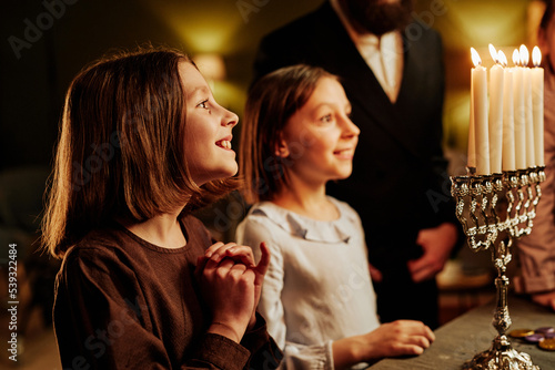 Side view portrait of smiling jewish girls looking at Menorah candle during Hanukkah celebration, copy space