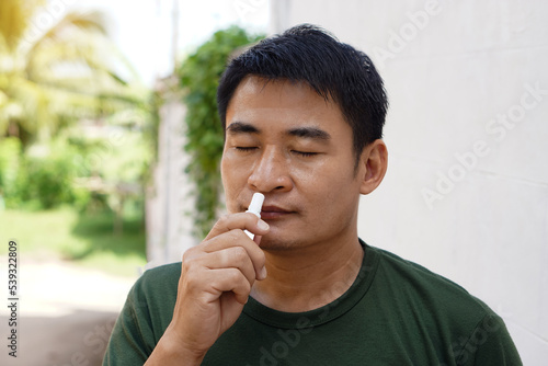 Asian man stands outdoor, feel dizzy and faint, smells inhaler to relieve. Concept : health problem, sickness and remedy. Increases freshness, reduces dizziness and stuffy nose. self take care. 