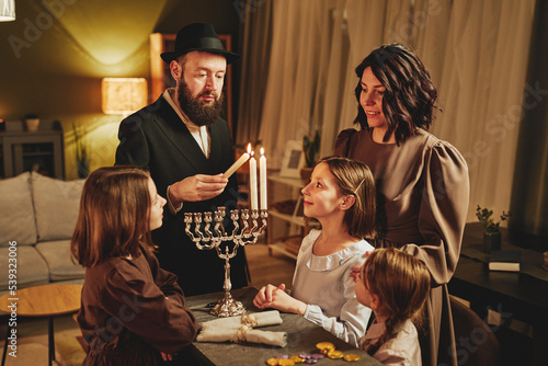 Fényképezés Portrait of orthodox jewish family lighting menorah candle together during Hanuk