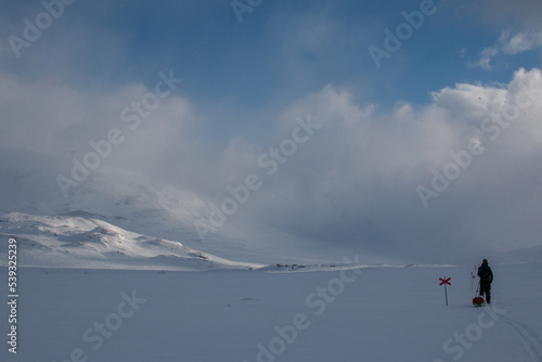 A skier with a sled is approaching Alesjaure mountain hut on Kungsleden trail, Lapland, Sweden