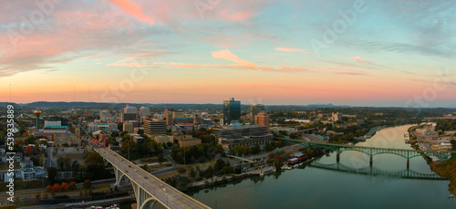 aerial shot of the Henley Street Bridge and Gay Street Bridge over the Tennessee River surrounded by autumn colored trees, lush green trees and office buildings with powerful clouds at sunset