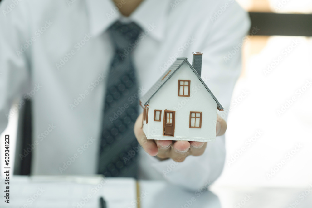 Real estate agent holding house model and keys to consult client. Real estate agent holding house model and keys to consult client.
