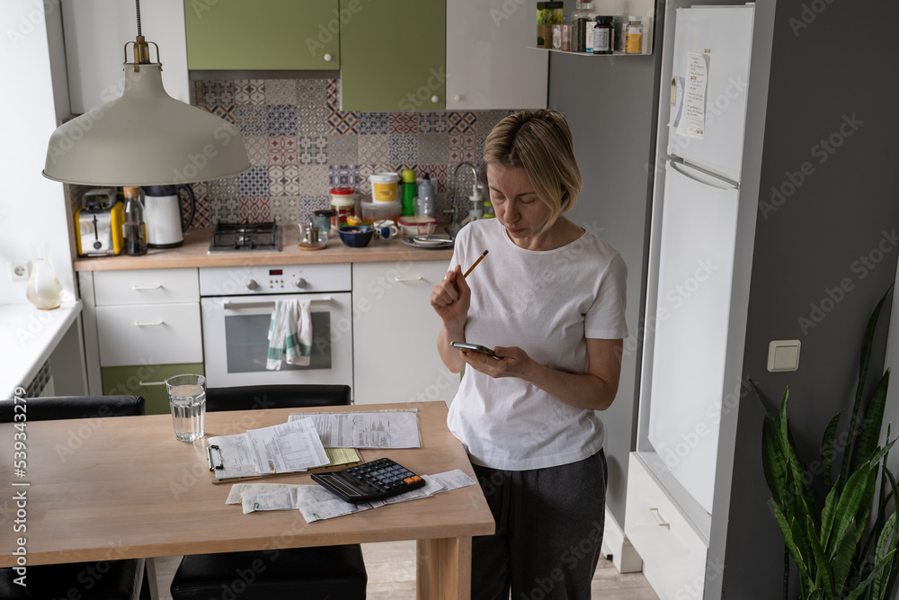 Middle-aged woman looks at phone and searches phone number of hotline. Mature female tries to figure out problems with electricity bills and reads information about payment. Family budget. Middle-aged woman looks at phone and searches phone number of hotline. Mature female tries to figure out problems with electricity bills and reads information about payment. Family budget.