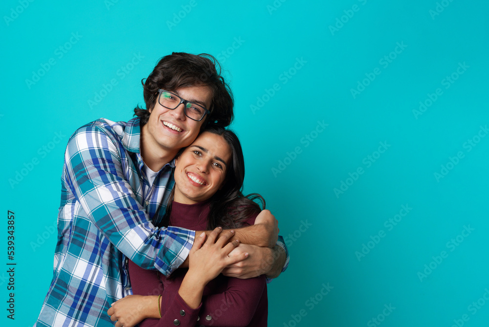 Fototapeta premium Happy couple in love hugging, embracing each other; casual wear, teenage years, fresh relationship; teal studio background