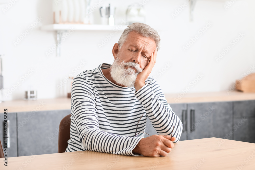 Thoughtful mature man sitting at table in kitchen Thoughtful mature man sitting at table in kitchen