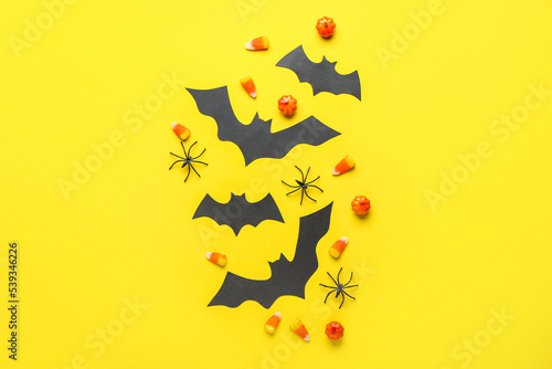 Paper bats with Halloween treats and spiders on yellow background