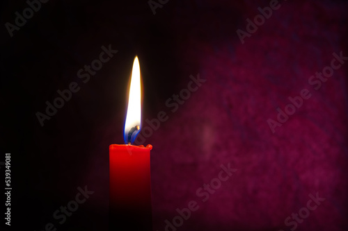 Single red candle burning alone in the dark red