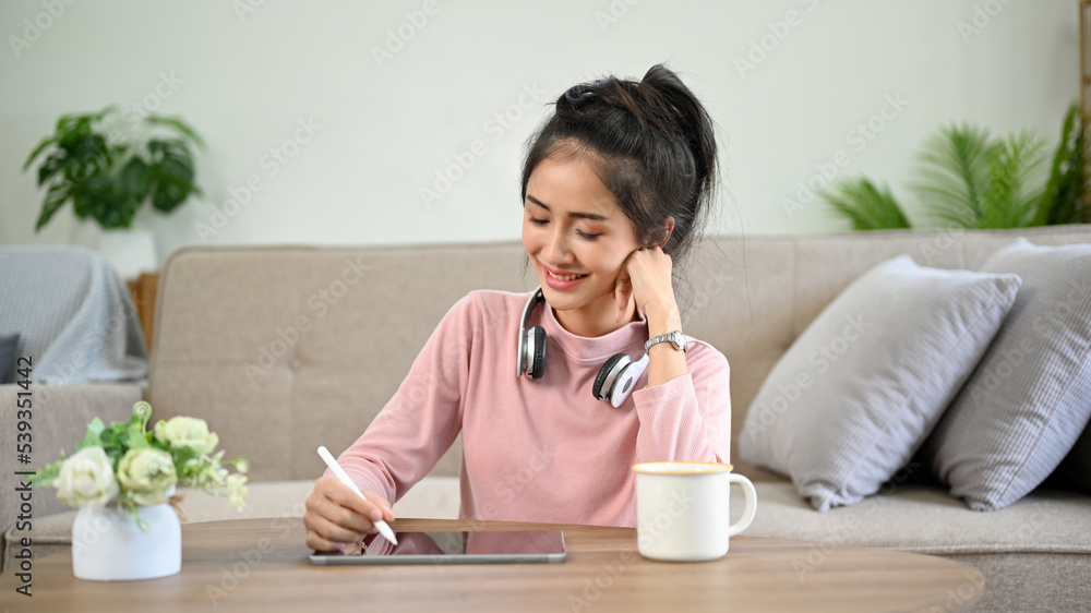 Pretty Asian girl using her tablet, sitting at her coffee table in her living room. Pretty Asian girl using her tablet, sitting at her coffee table in her living room.