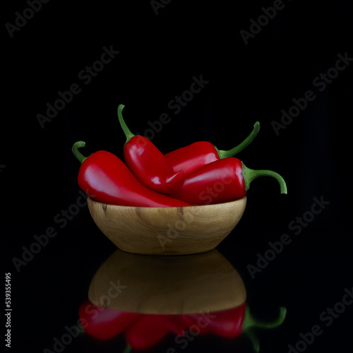 Red hot chili pepper in a wooden bowl on a black background. Photo.