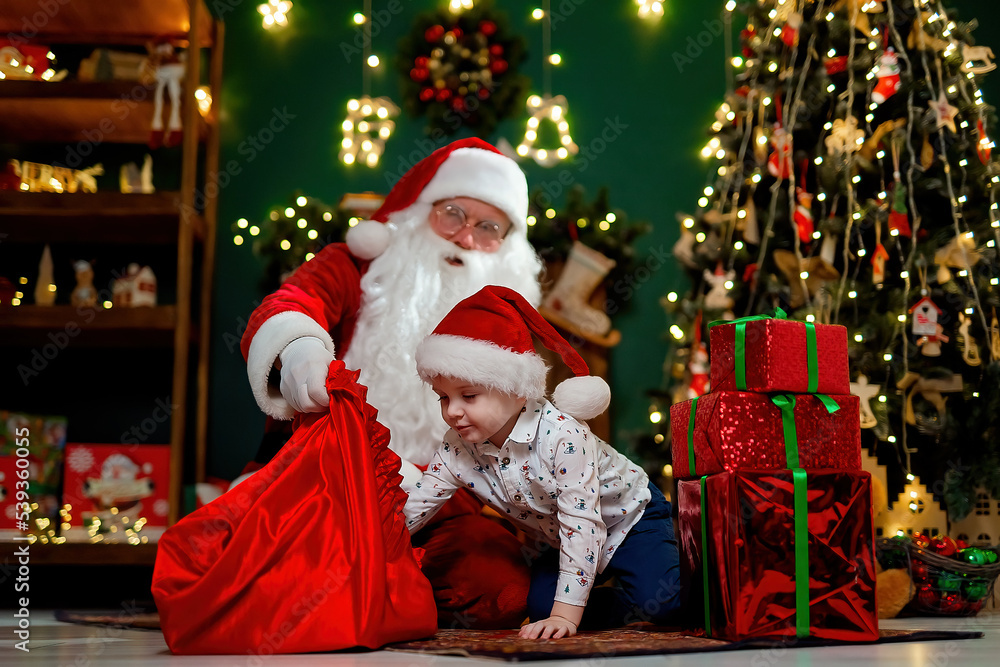 Little boy in Santa's hat takes out presents from Santa claus sack. Christmas time. New Year concept