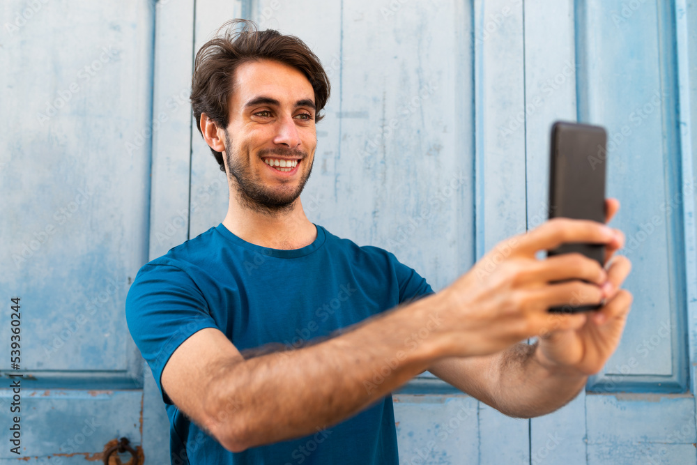 Young caucasian man taking a selfie using mobile phone outdoors. Young caucasian man taking a selfie using mobile phone outdoors.