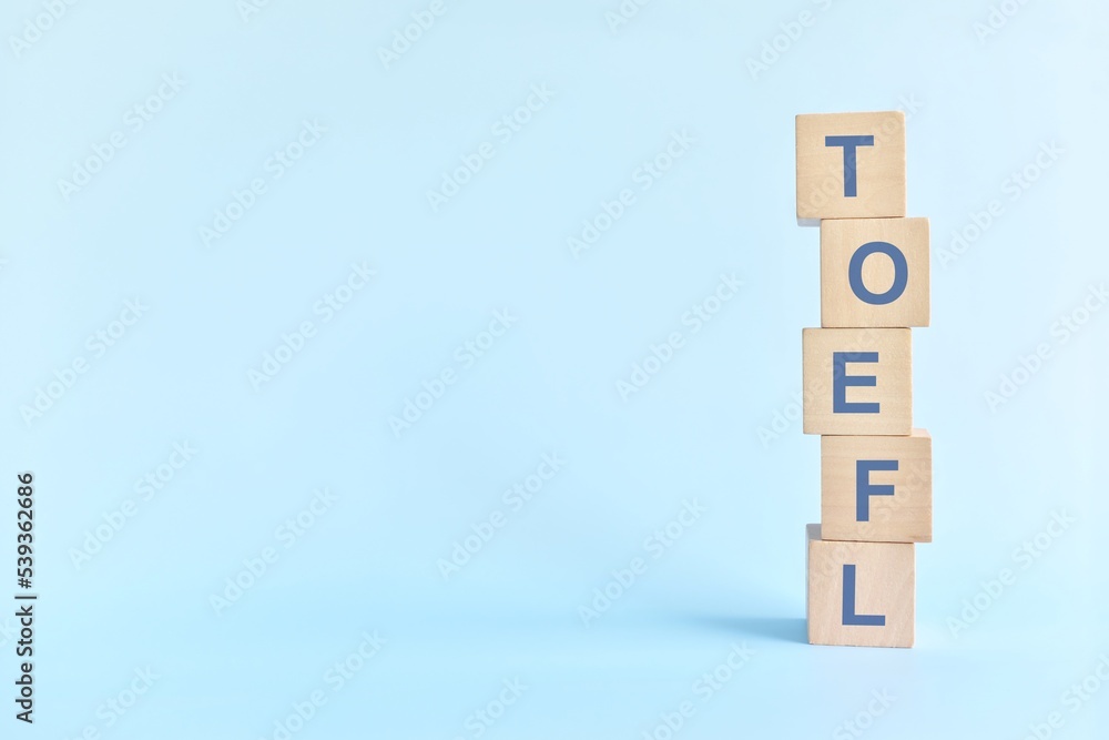TOEFL or test of english as a foreign language testing system exam concept. Wooden blocks typography flat lay on blue background.