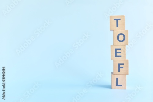 TOEFL or test of english as a foreign language testing system exam concept. Wooden blocks typography flat lay on blue background. 
