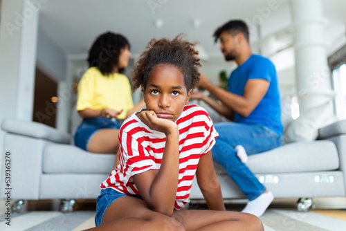 Family Conflicts. Sad little black girl looking away while her parents arguing in the background, upset child doesn't want to hear quarrel, stressed kid sitting alone, selective focus