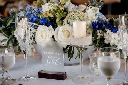 Sweetheart sign on table with blue and white wedding floral centerpiece on white table cloth surrounded by place settings and glassware. blue hydrangeas white roses horizontal no people photo