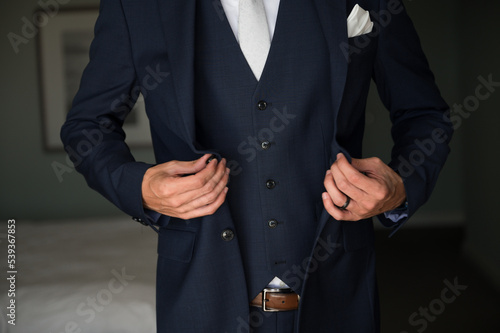 Groom getting ready for wedding buttoning navy suit jacket close crop no face