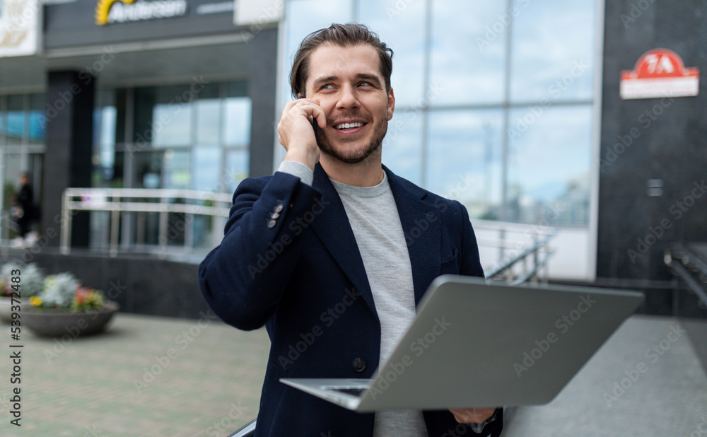 satisfied and successful man 35 years old in business clothes speaks on the phone with a laptop in his hands satisfied and successful man 35 years old in business clothes speaks on the phone with a laptop in his hands