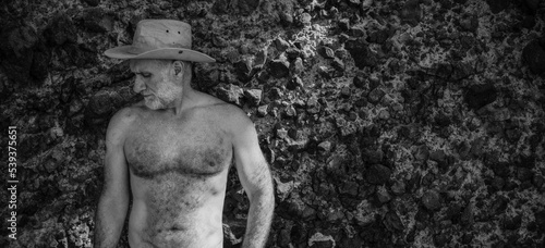 Monochrome of shirtless adult man in cowboy hat against rock photo