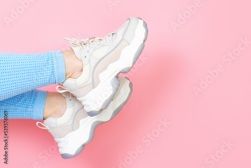 Female legs in blue pants and running shoes on pink background close-up with copy space.
