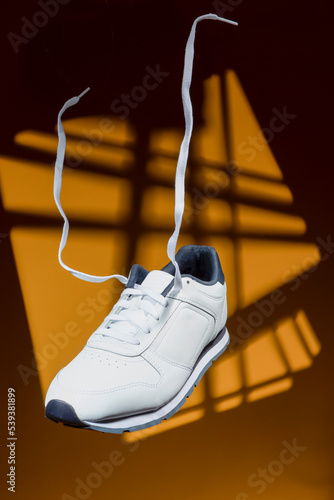 Fashion and Lifestyle Concepts. One New White Sneaker With Flying Shoelaces Placed Over Yellow Background With Triangle Sportlight.