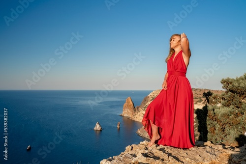 A woman in a red flying dress fluttering in the wind, against the backdrop of the sea.