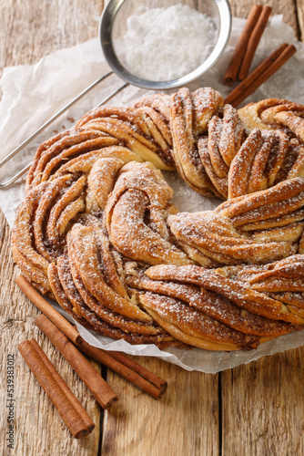 Estonian Kringle Cinnamon Braid Bread with powdered sugar closeup on the paper on the wooden table. Vertical photo