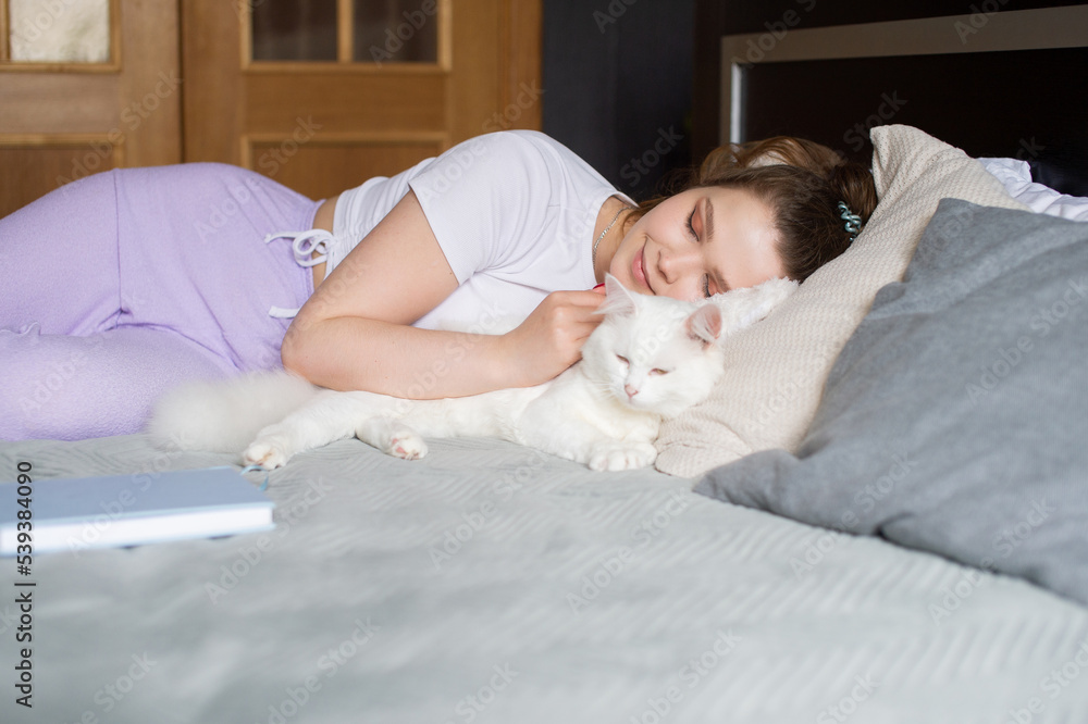 Cute girl sleeping on a bed next to a white cat Cute girl sleeping on a bed next to a white cat
