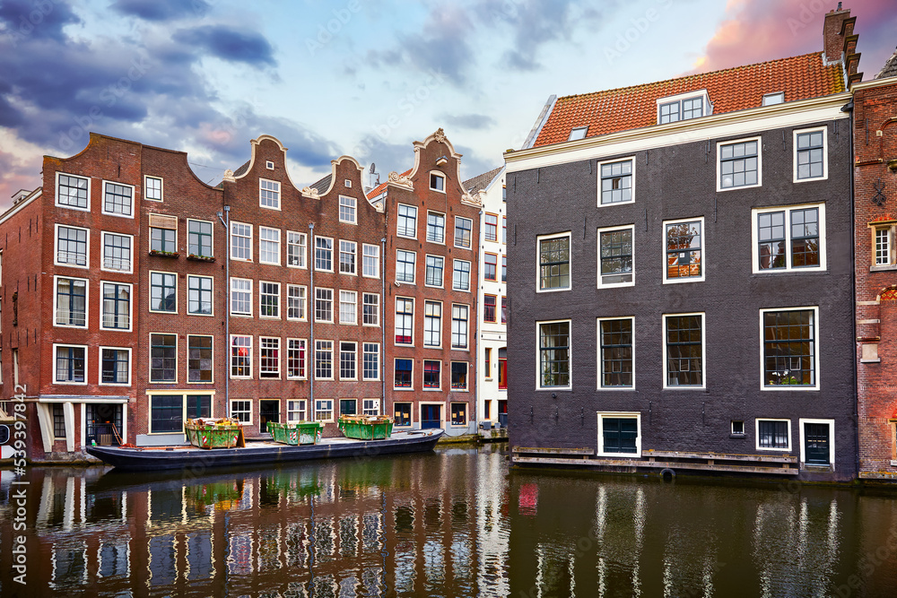 Red-light district in Amsterdam city picturesque landscape panorama evening town with pink sunset sky. Traditional brick houses with windows ove water.