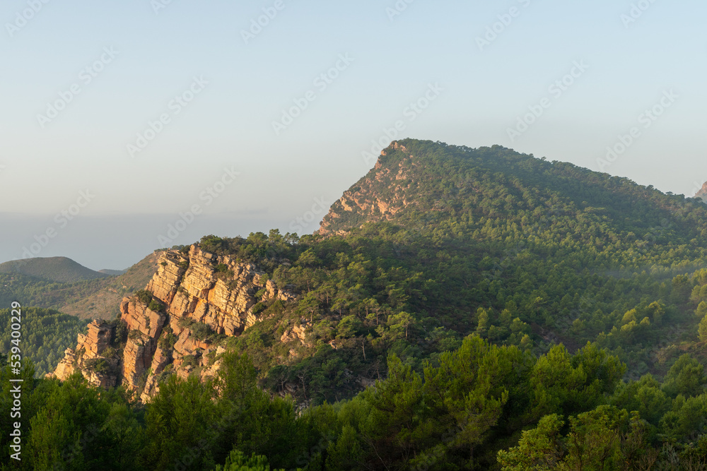 Beautiful landscape with mountains, trees and a bit of fog on the side while the sun's rays dye the rocks in the Valencian community, Spain