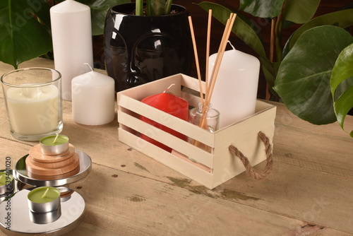 Drewniane pudełko ze świeczkami i patyczkami zapachowymi na drewnie z roślinami w tle