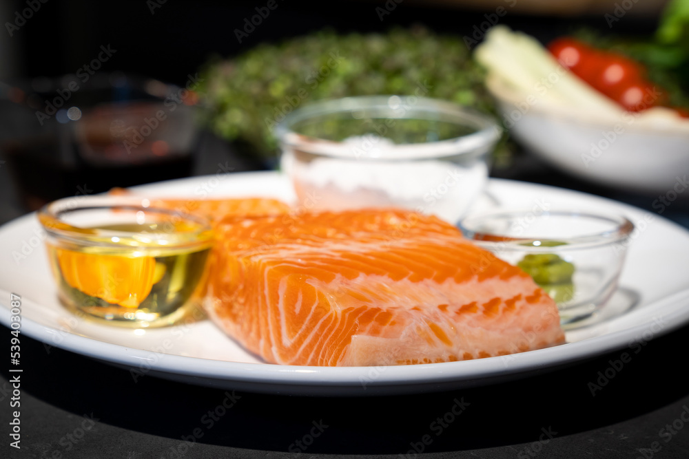 Close up to Salmon Trout steak, Raw fillet of sea fish on white dish with salt, oil, and wasabi cream in studio light on dark background. Close up to Salmon Trout steak, Raw fillet of sea fish on white dish with salt, oil, and wasabi cream in studio light on dark background.
