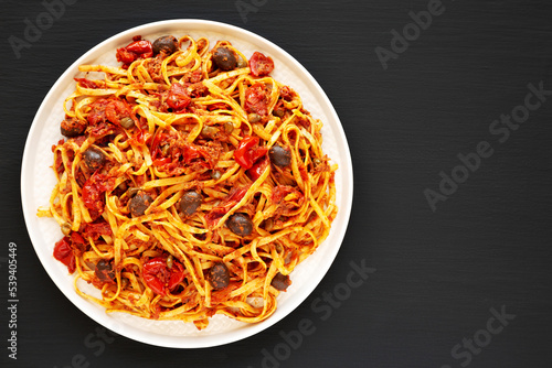 Homemade Tuna Linguine Pasta with Tomatoes, Olives and Capers on a Plate on a black background, top view. Overhead, from above, flat lay. Copy space.