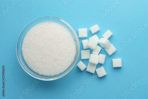 Cukier biały w miseczce i rozsypany w kostkach na niebieskim