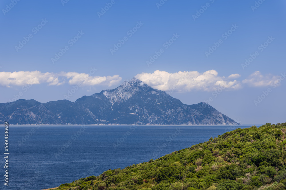 Abundant juicy green vegetation on one side of Singitic Gulf, and opposite the world-famous historic Mount Athos with traditional snow-white clouds round-dancing at its top, Chalkidiki, Greece.