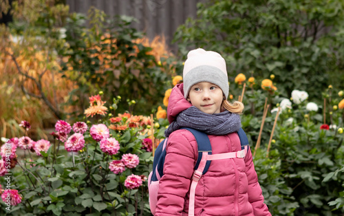girl in a pink jacket and a hat for a walk in the park among the flowers in autumn