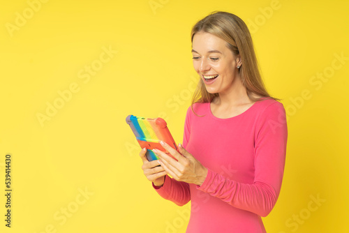 Smiled attractive young girl holding digital tablet pc with colored cover reading online news  happy woman makes internet shopping online using gadget pc isolated on yellow background