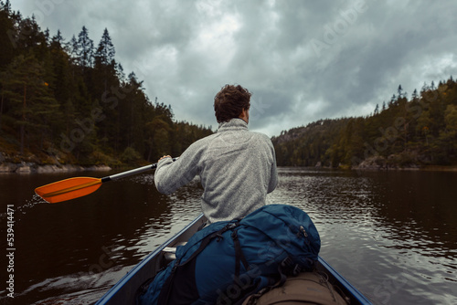 A caucasian man canoeing on a lake in a forest with dramatic clouds reflecting in the water.