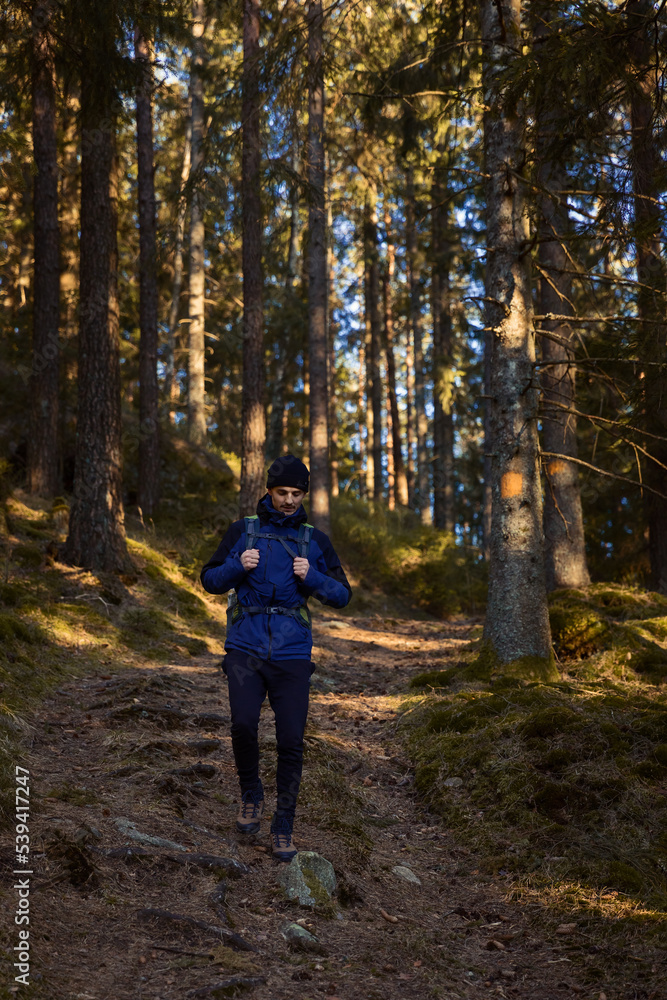 A caucasian man with a backpack hiking in the forest on a path with sun shinning. A caucasian man with a backpack hiking in the forest on a path with sun shinning.