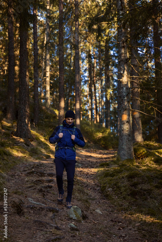 A caucasian man with a backpack hiking in the forest on a path with sun shinning.