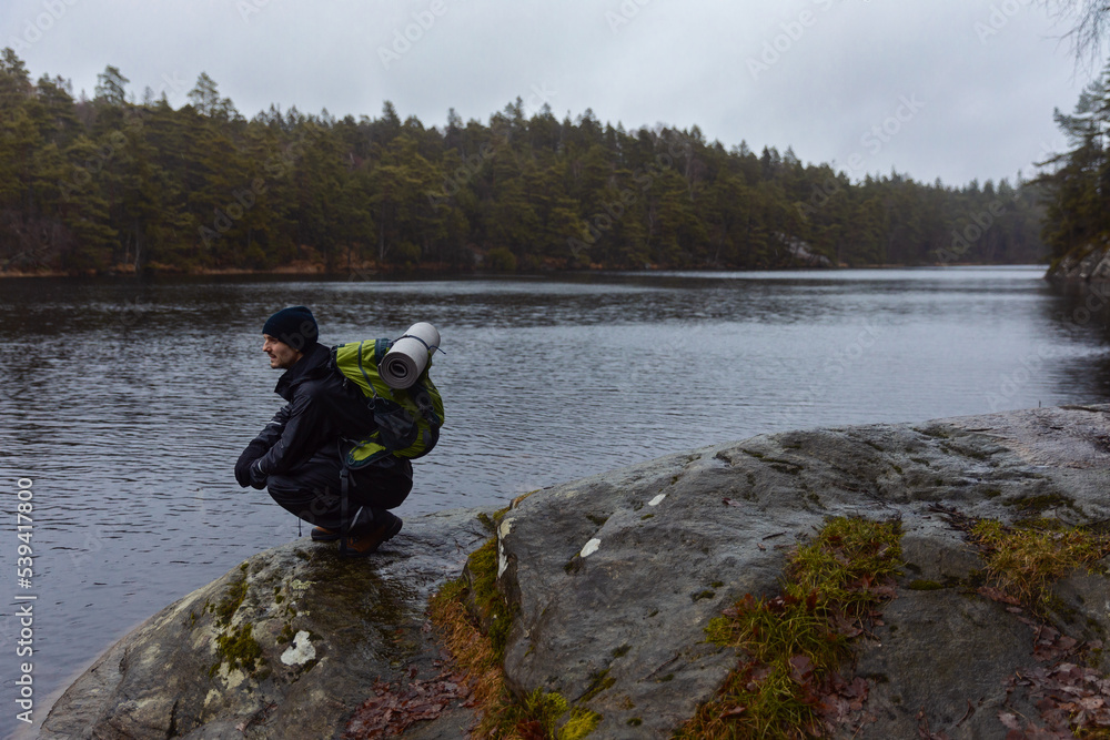 A caucasian man sitting on a rock with a backpack by a lake in a forest. A caucasian man sitting on a rock with a backpack by a lake in a forest.