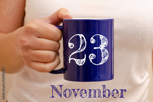 The inscription on the blue cup 23 november. Cup in female hand, business concept