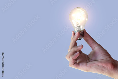 hand holding an incandescent light bulb isolated on blue background. Generate great ideas. illuminated light bulb.