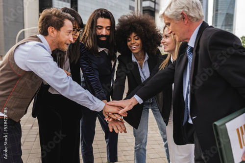 Multiracial business team joining hands together while standing outdoors in front of office building