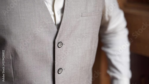Man buttoning up simple gray waistcoat over white shirt, close up.