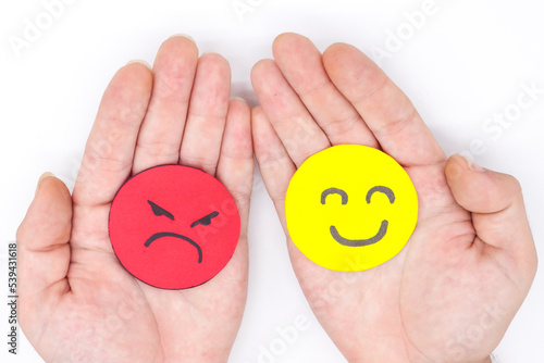 hands holding two angry and happy faces of yellow and red paper on a white background. Concept of envy, fights, anger, social problems, avoidance of problems