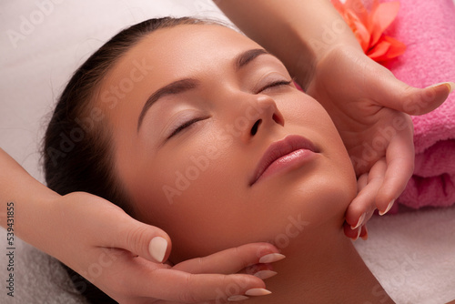 Beautiful caucasian woman enjoying facial massage with closed eyes in sunny spa salon. Relaxing treatment in medicine